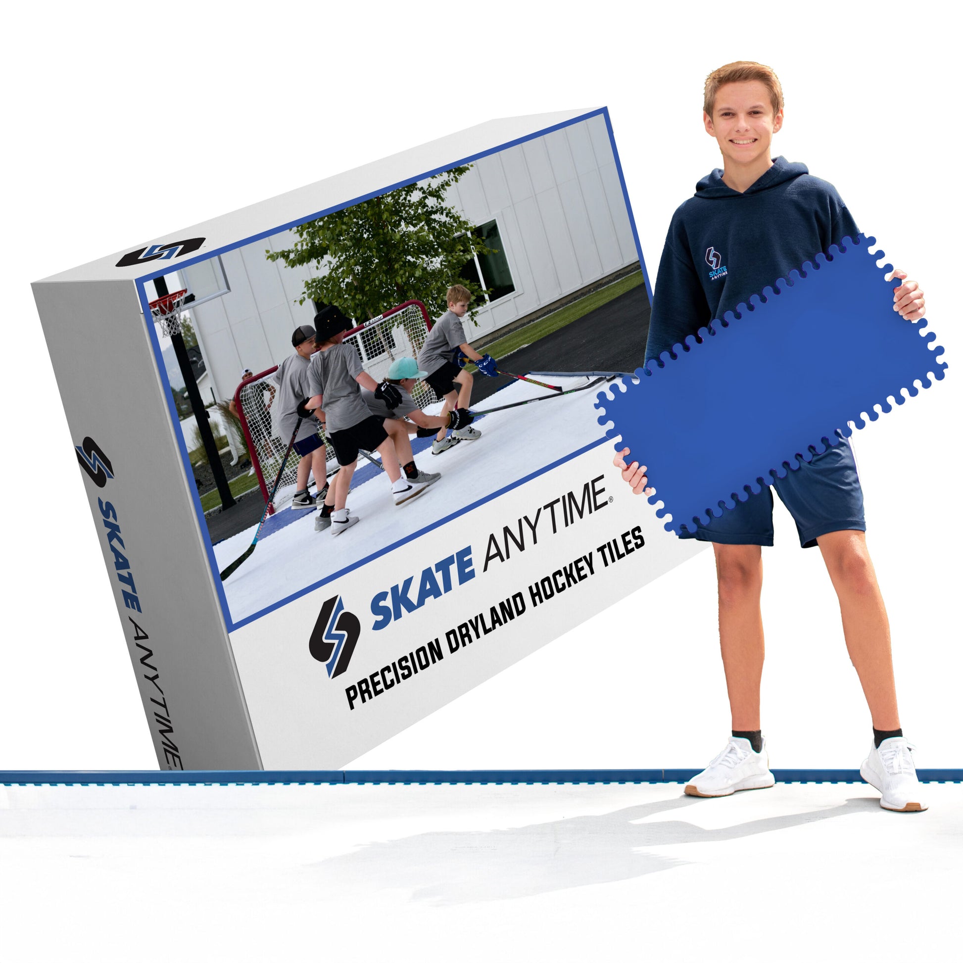 A man stands next to a large product box for 'Skate Anytime' precision dryland hockey tiles, holding a blue interlocking tile. The box features a photo of kids playing on an outdoor rink and the brand logo 'Skate Anytime'.