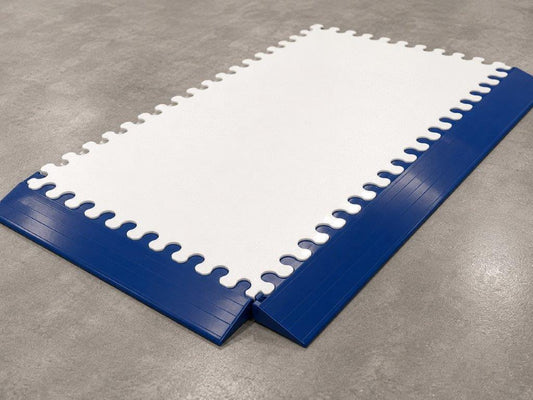 Blue and white interlocking foam play mats with wavy edges, arranged on a gray concrete floor.