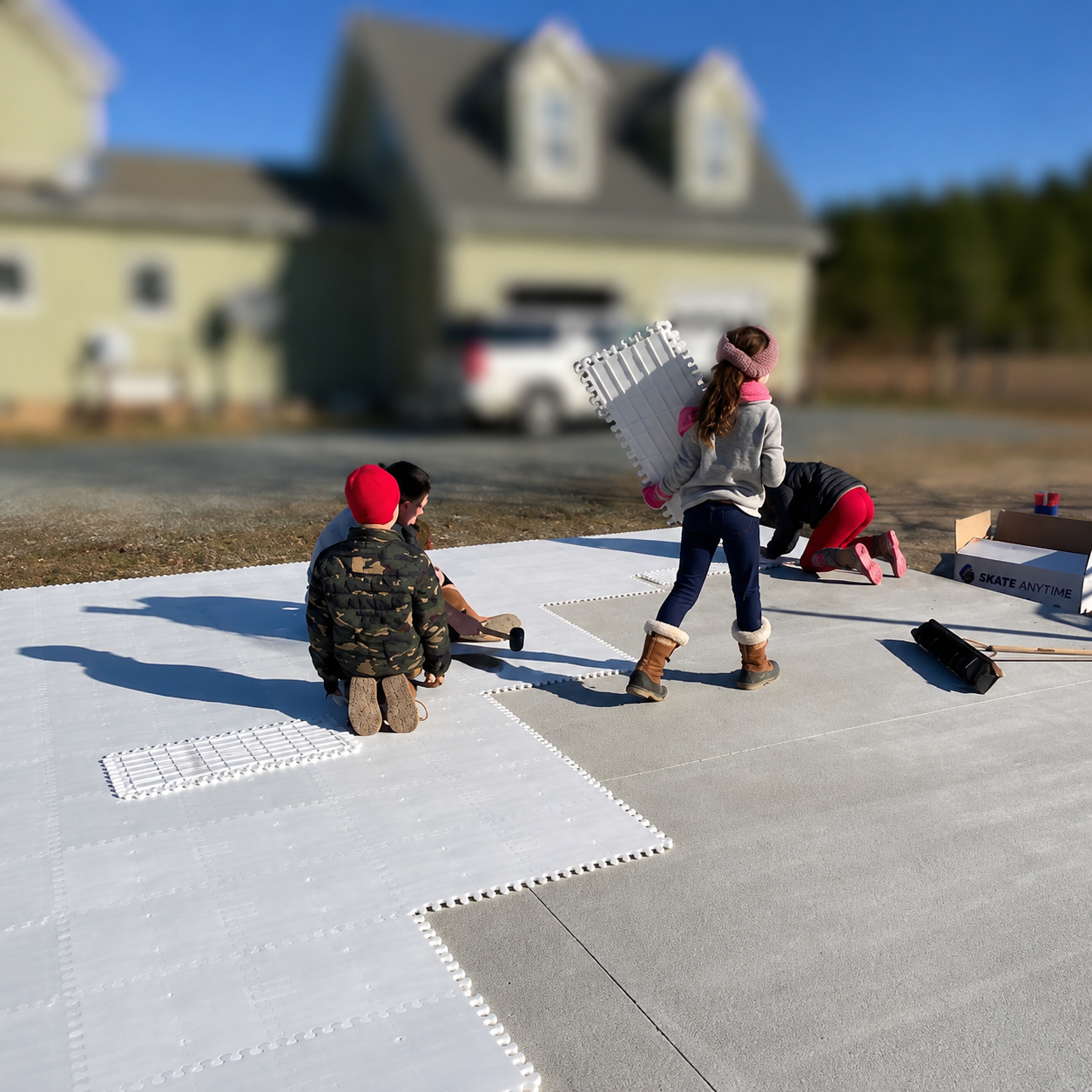 Three children are assembling white interlocking foam floor mats outdoors in a backyard, with a house and trees blurred in the background.